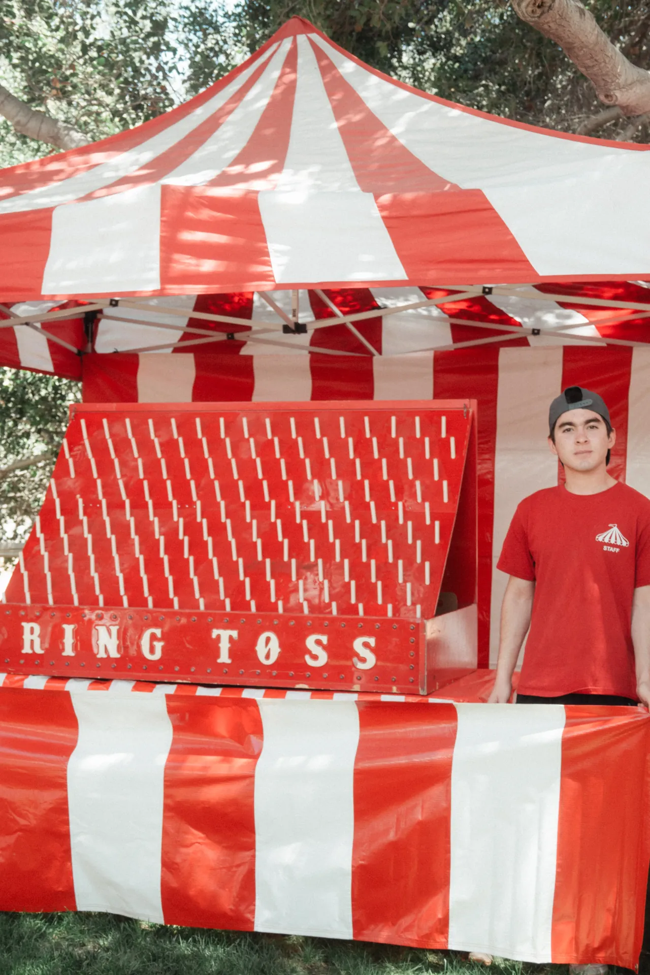 Guests throwing rings at a classic carnival ring toss game while an attendant watches, set against a striped backdrop