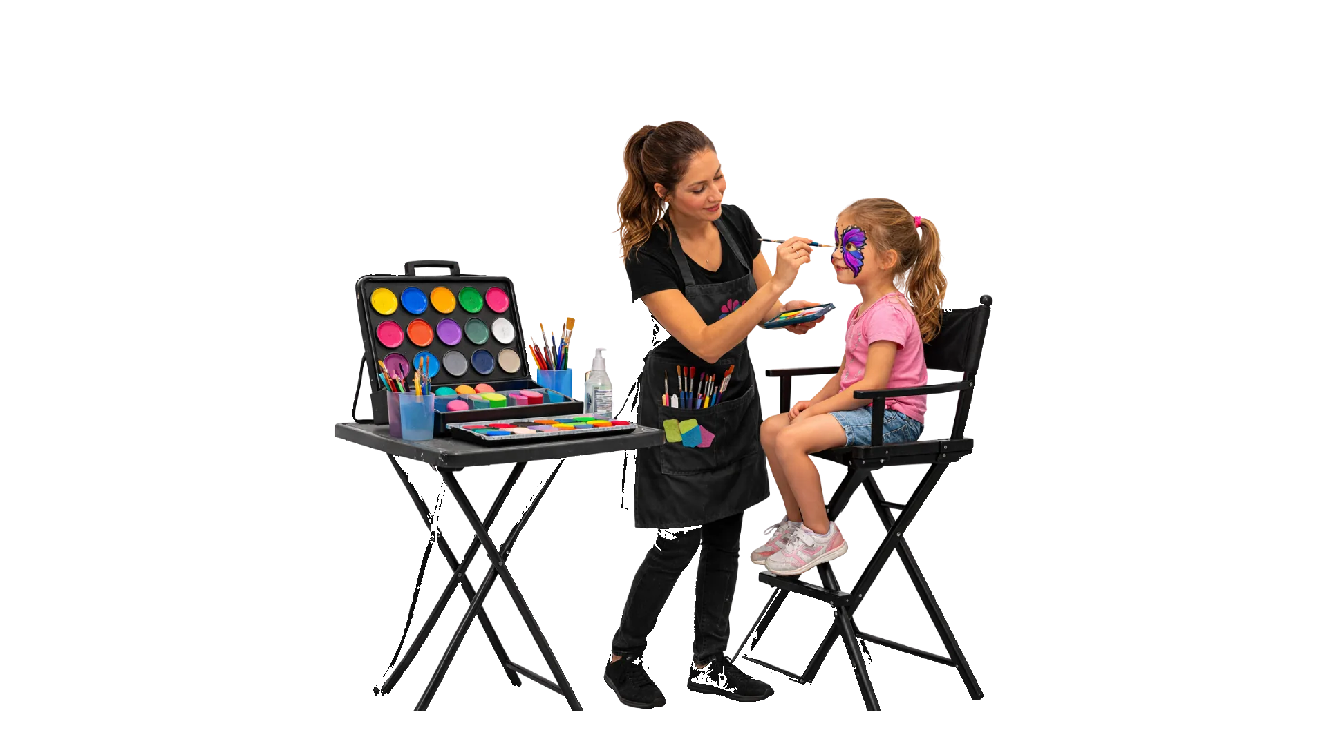 A face painter at a small table painting a butterfly on a child's cheek while a balloon-twisting artist works the line behind in Commerce, CA
