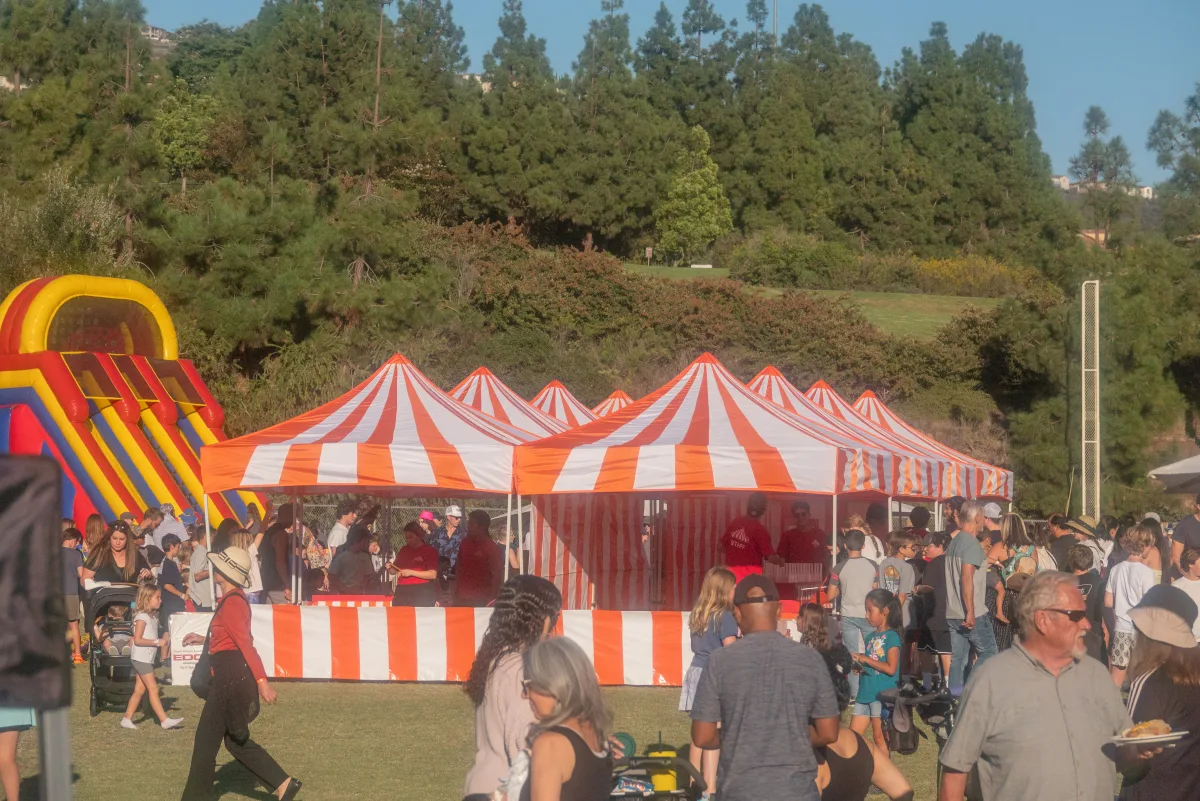Orange-and-white striped carnival booths set up on a grass field at an outdoor community event, one of the three Halloween booth colors available for La Cañada Flintridge