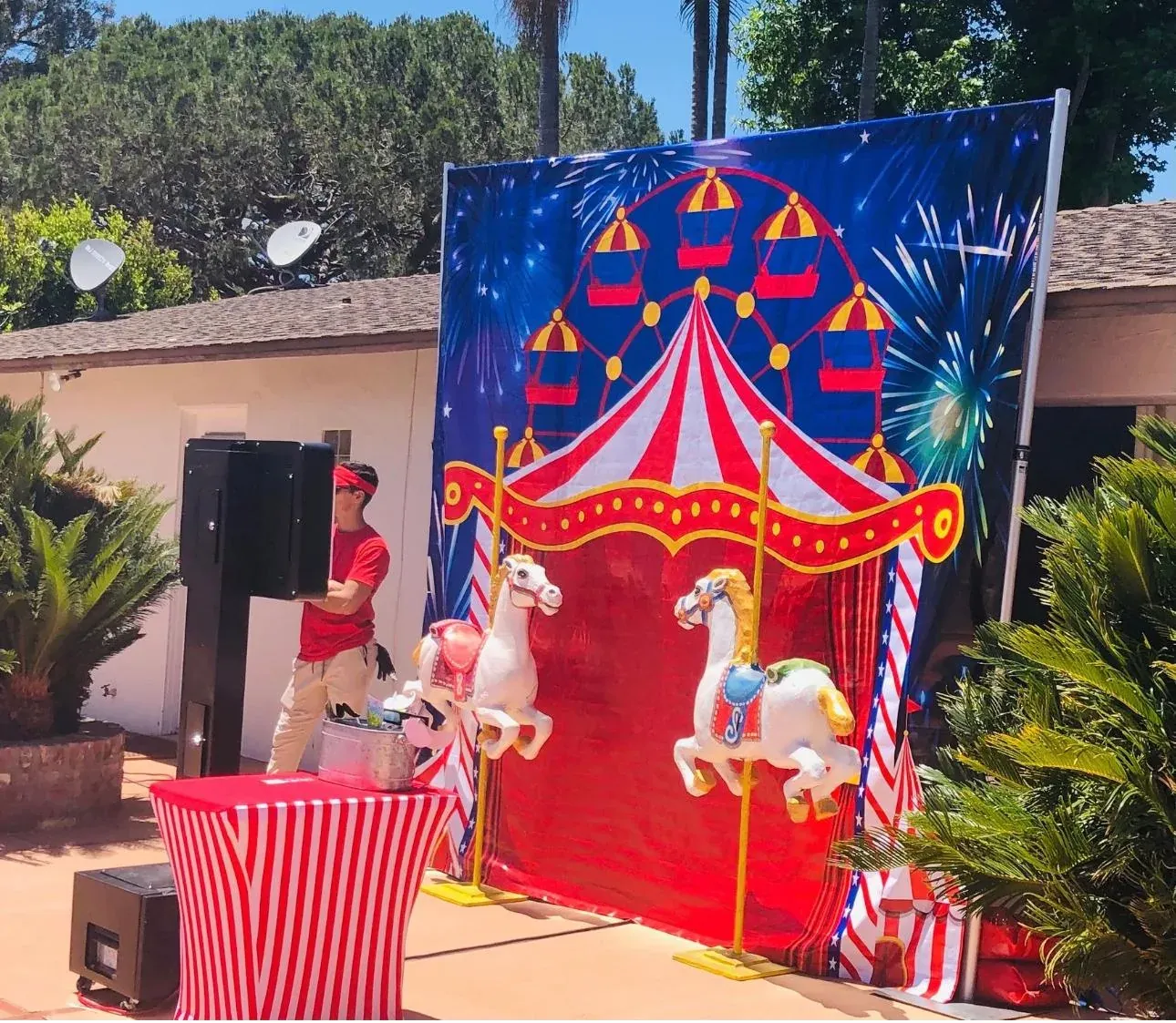 A backyard birthday party with red-and-white carnival booths, a popcorn machine, and children playing prize games near a cake table in Commerce, CA