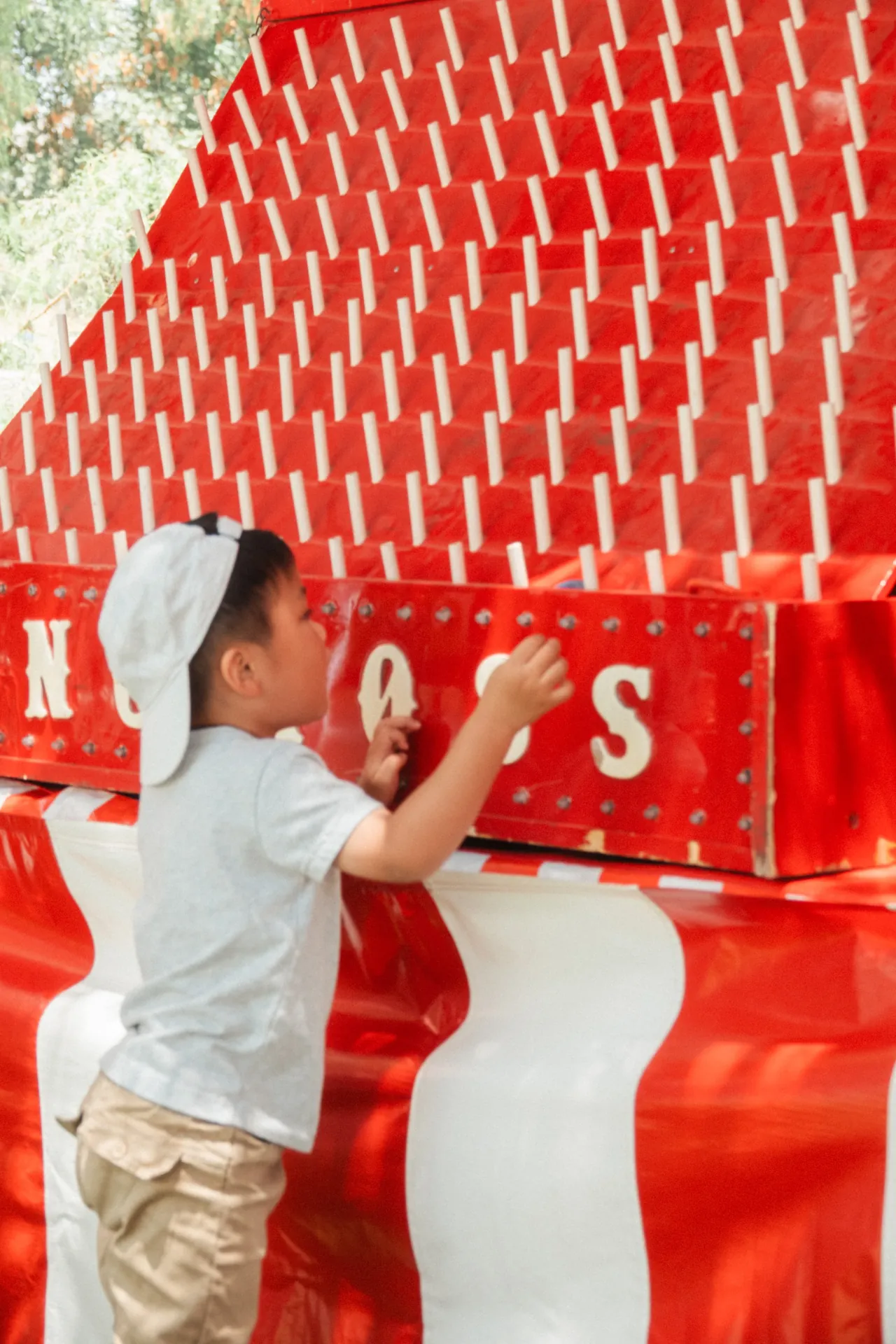 A row of carnival game booths set up on grass at a community festival with kids playing ring toss and an attendant handing out prizes
