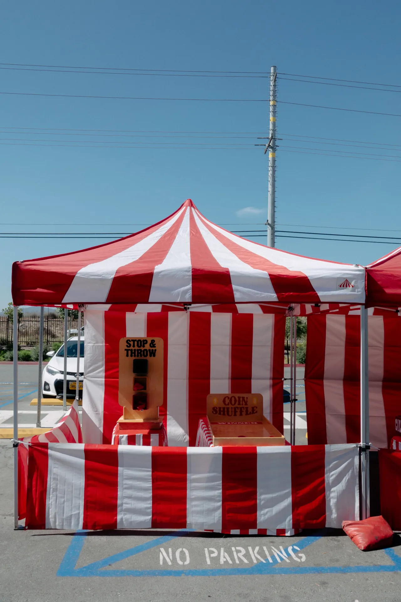 Employees and children playing carnival games at staffed striped booths during a corporate outdoor event, with a cotton candy attendant handing out treats in the foreground
