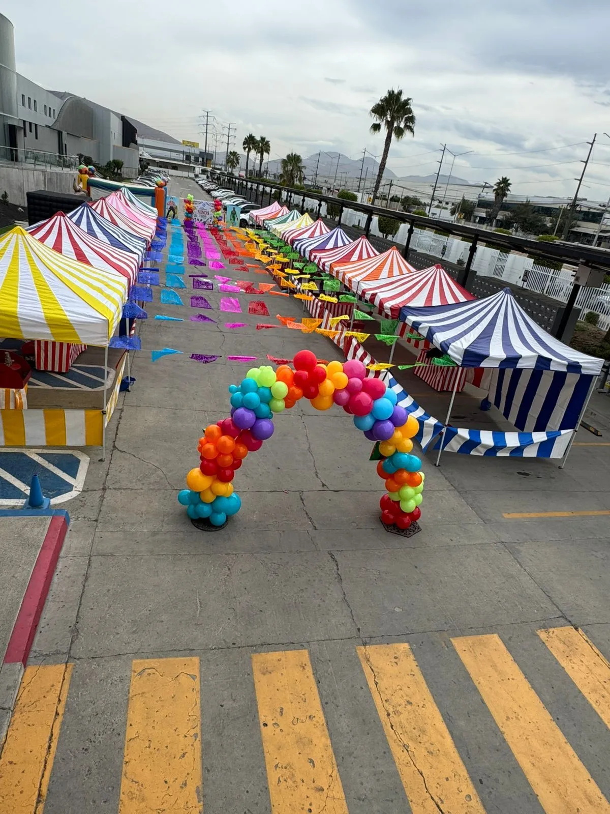 A grand opening setup outside a retail storefront with red-and-white striped carnival booths, a balloon arch over the entrance, and families gathered in the parking lot in Carson, CA