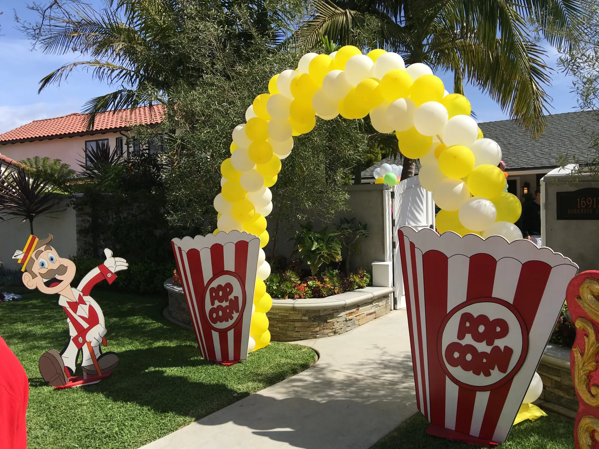 A ribbon-cutting ceremony outside a new storefront with red-and-white striped carnival booths set up along the parking lot perimeter and a crowd gathered at the entrance